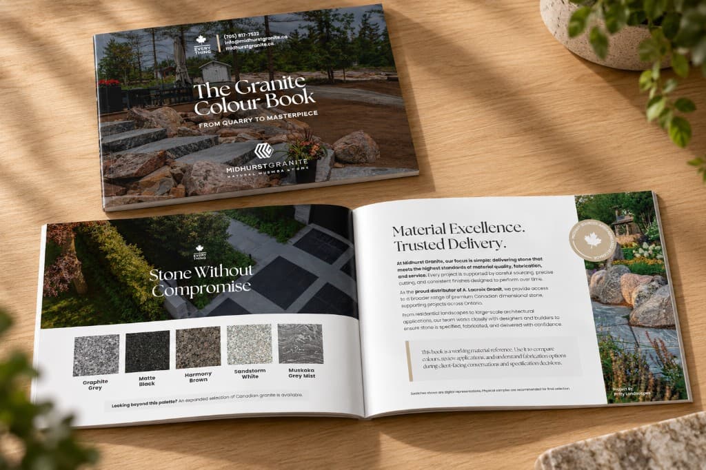 The Granite Colour Book on a light wood table: the closed cover above an open spread of granite colour chips and a landscaping photograph.