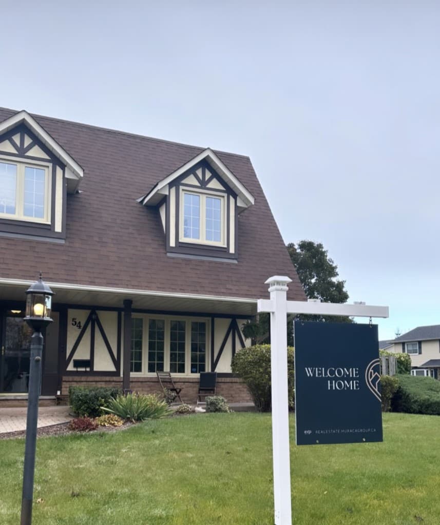 A navy Welcome Home lawn sign on a white post in front of a cream Tudor-style house.