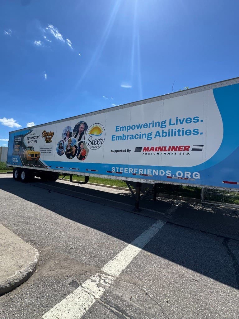 The Steer Friends trailer from a short distance on a paved lot: the white and blue wrap, circular photos, and the wordmark against a bright sky.