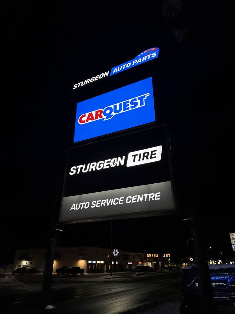 Roadside pylon sign at night with three lit panels: Sturgeon Auto Parts at the top, Carquest in the middle, and Sturgeon Tire Auto Service Centre at the bottom.