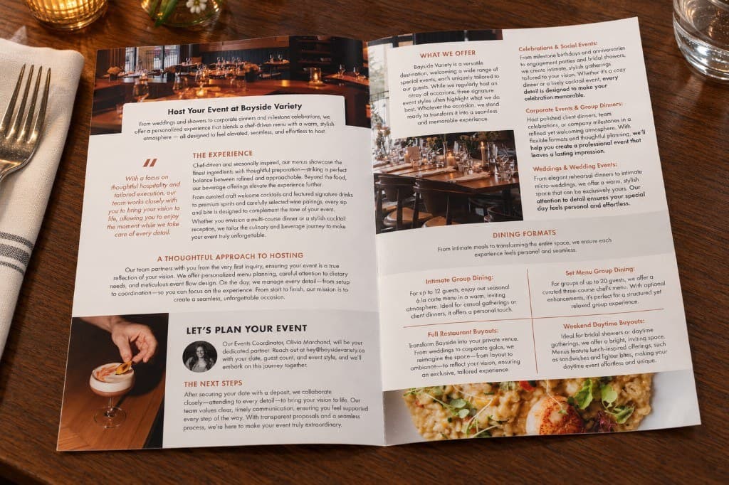 An open Bayside Variety event brochure on a dark table: columns of event information, a dining-room photograph, and a salad photograph.