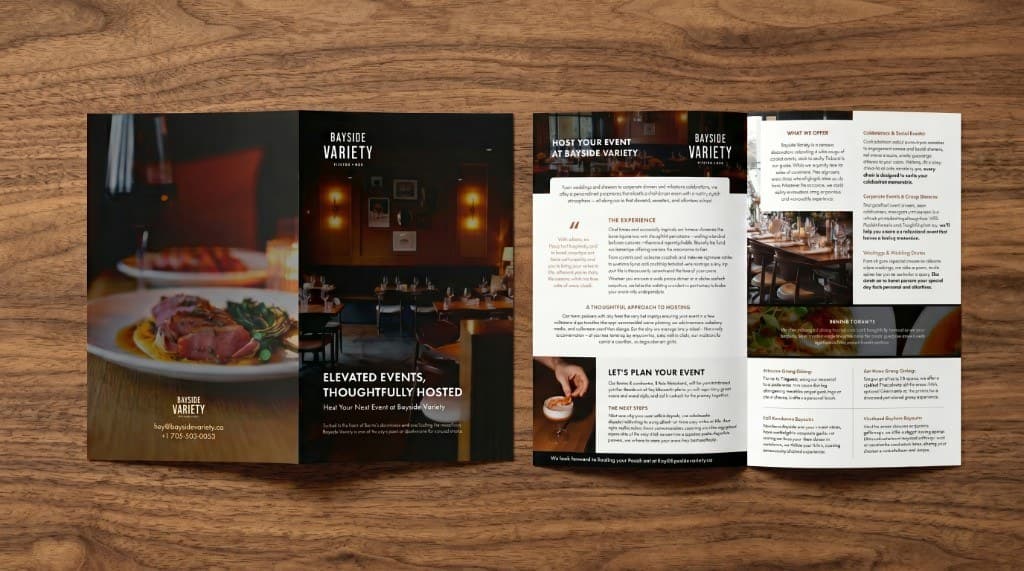 A Bayside Variety event brochure laid flat on wood: a dark cover with a dining-room photograph, and an open interior of headings, columns, and photographs.
