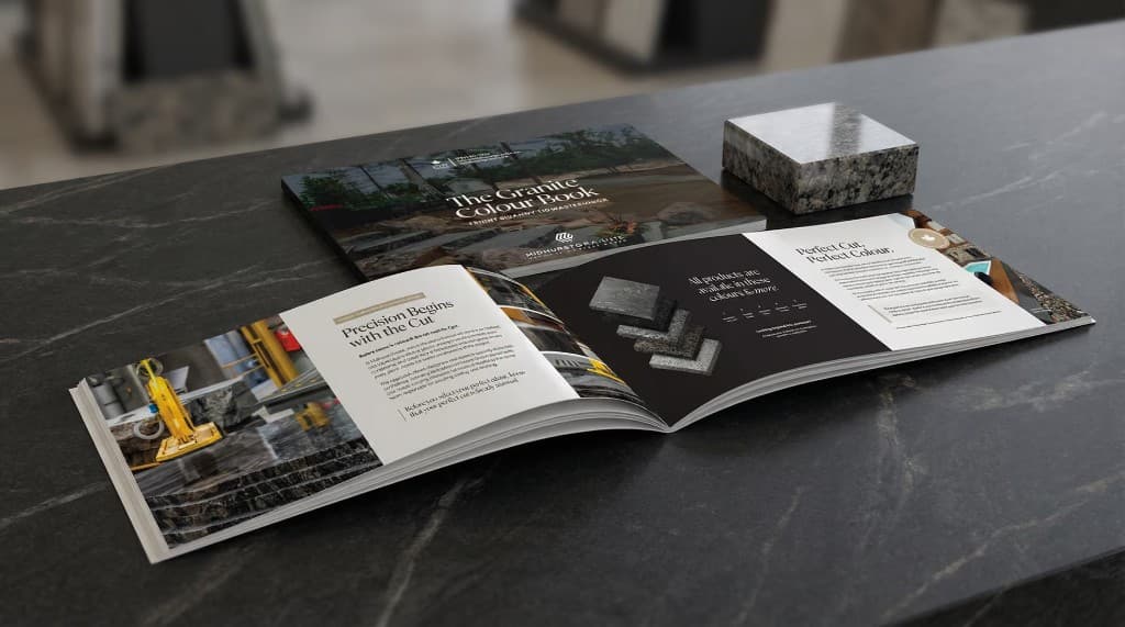 The Granite Colour Book open on a dark stone counter, with the closed cover and a granite sample block beside it.