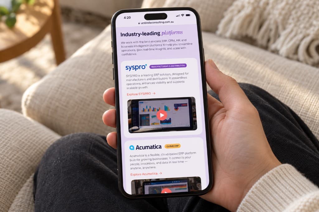A phone held over a cream sofa, showing Umbrella Consulting software platform listings with a video still on the screen.